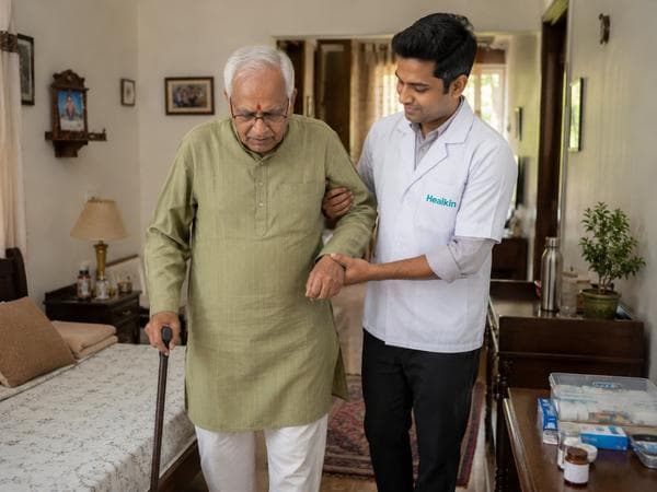 A Healkin attendant helping an elderly patient walk at home